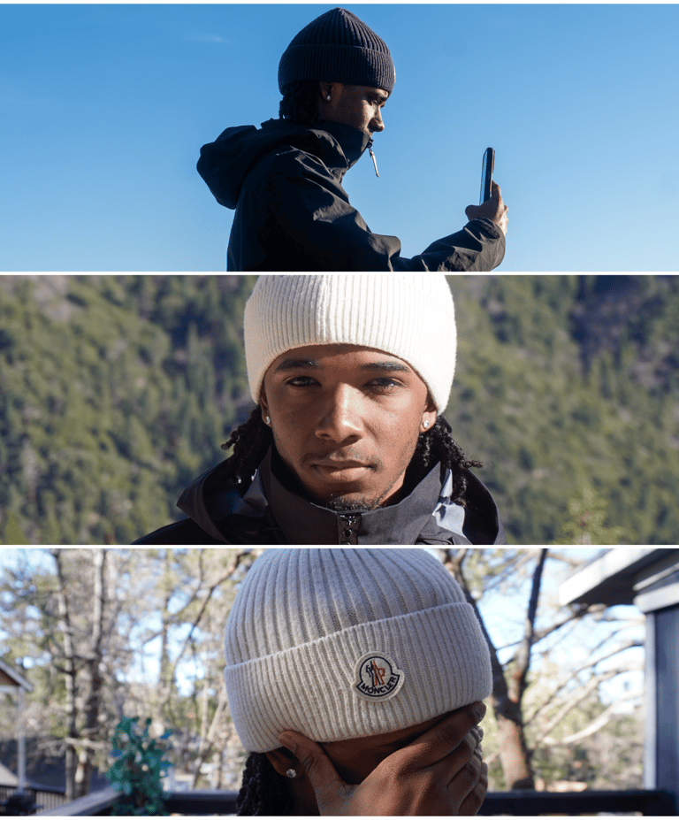 A man wearing a Moncler knit beanie and winter jacket takes photos in a mountain landscape.