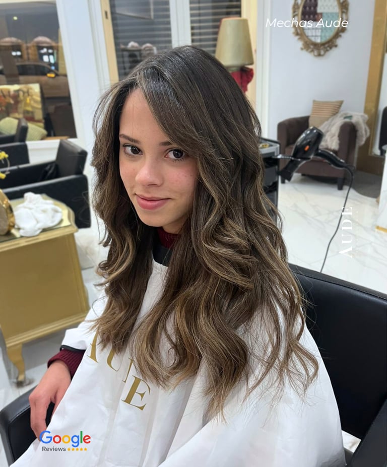 Young woman with long brunette hair and honey blonde balayage highlights styled in loose waves at a salon.