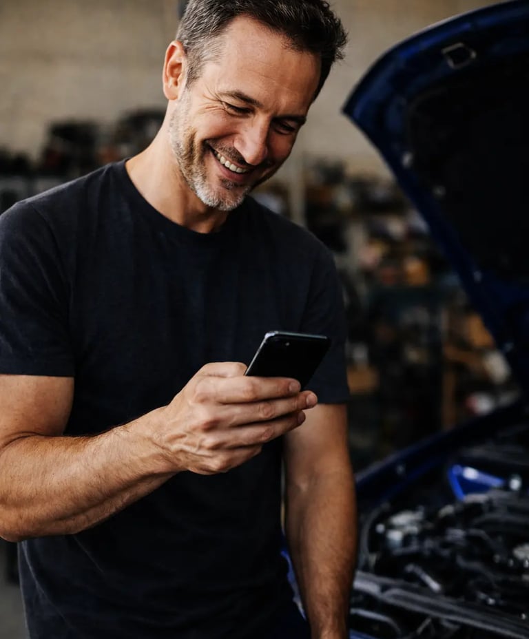 Meccanico sorride guardando lo smartphone, supporto Hulemex online che accompagna e spiega i prodott