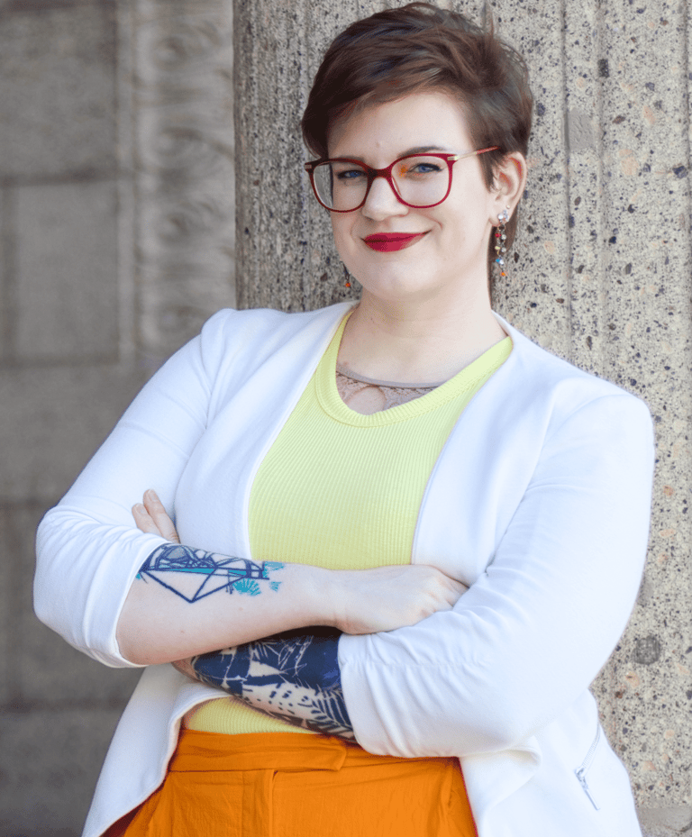 a photo of Swana Schuchmann with short hair, a white blazer and glasses, smiling