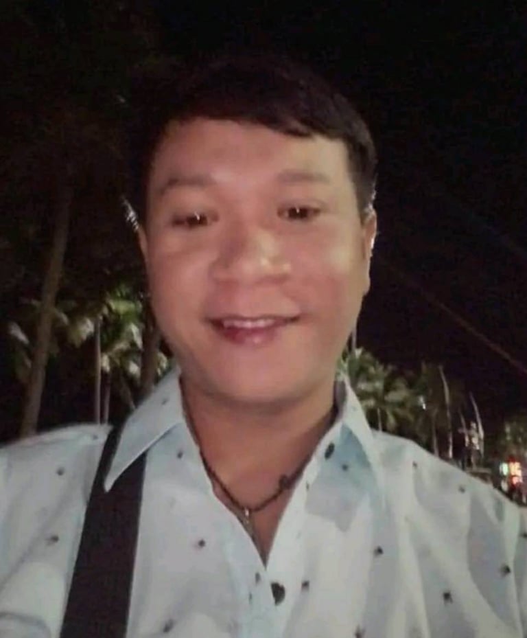 Male therapist smiling at night in Pattaya, Thailand, wearing a light shirt and shoulder bag.