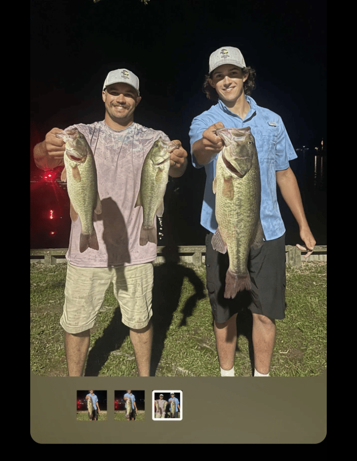 Two smiling men holding large largemouth bass caught during a night fishing trip by the lake.