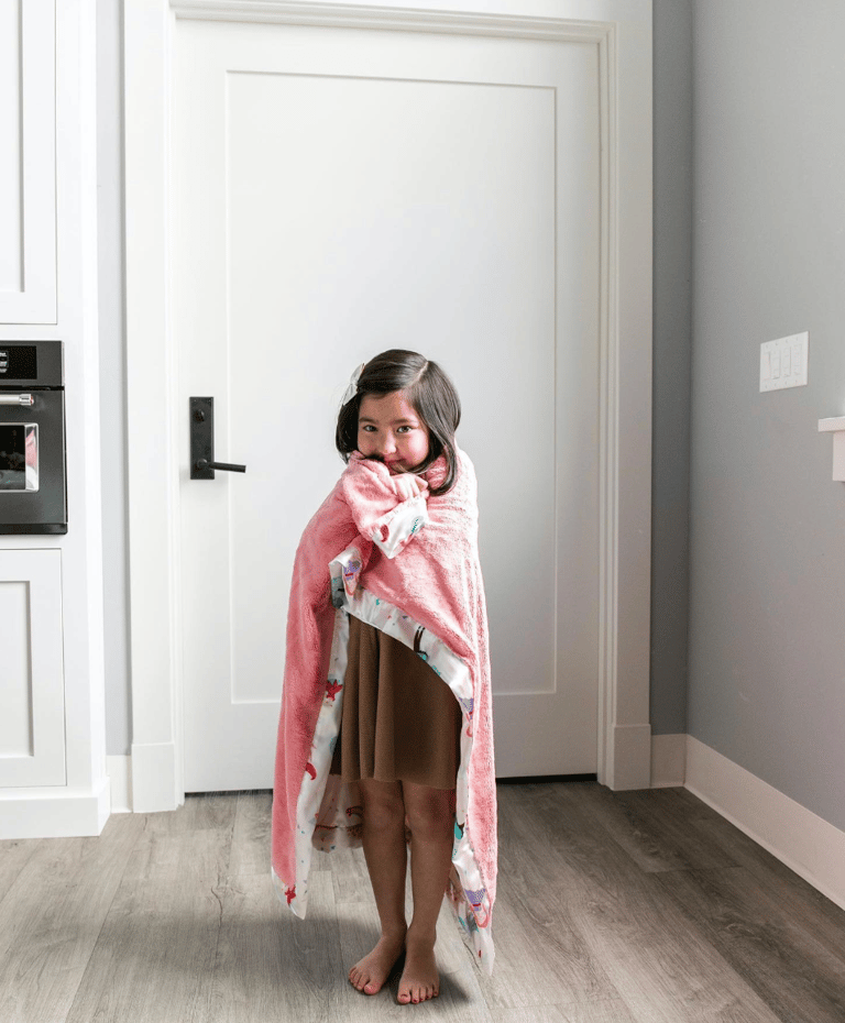 a little girl standing in a room with a pink blanket