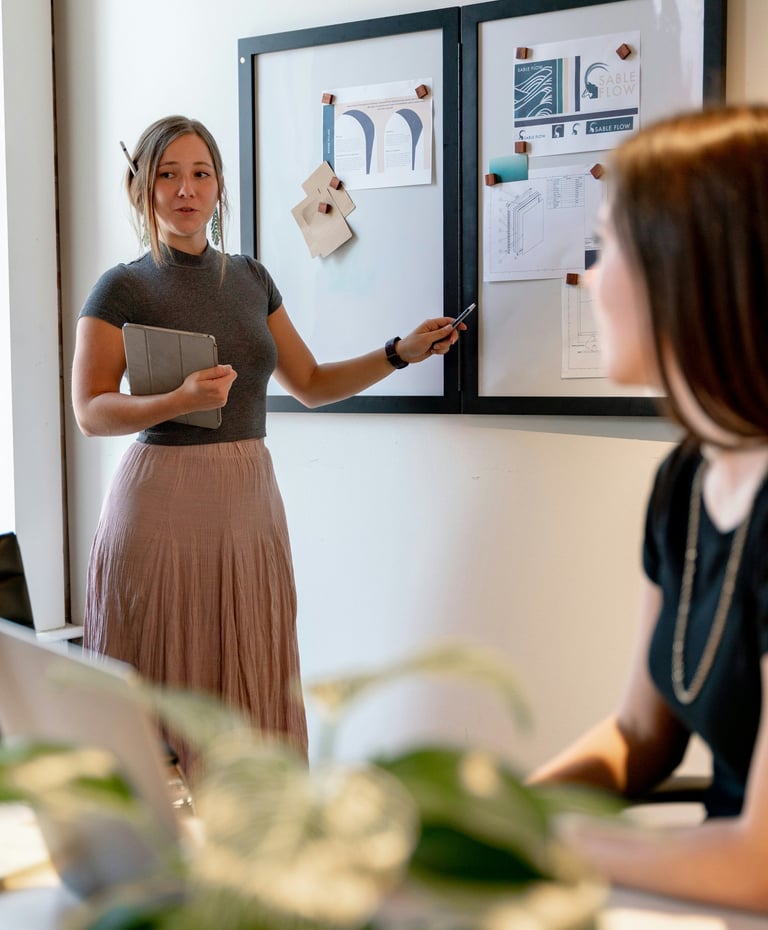 A young professional woman presents design concepts on a whiteboard during a creative office meeting.