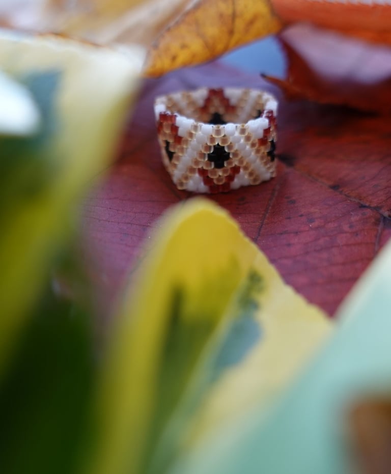 A ring made with Japanese seed beads on a table with some leaves around 