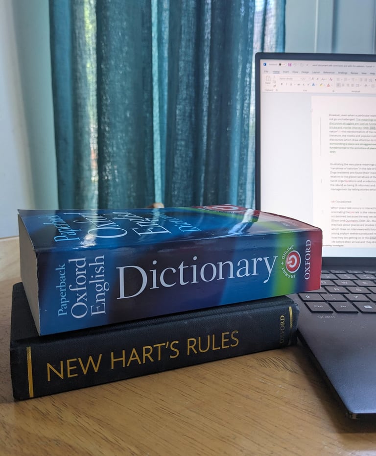 An Oxford English dictionary and New Hart's Rules style guide on a table next to a open laptop.