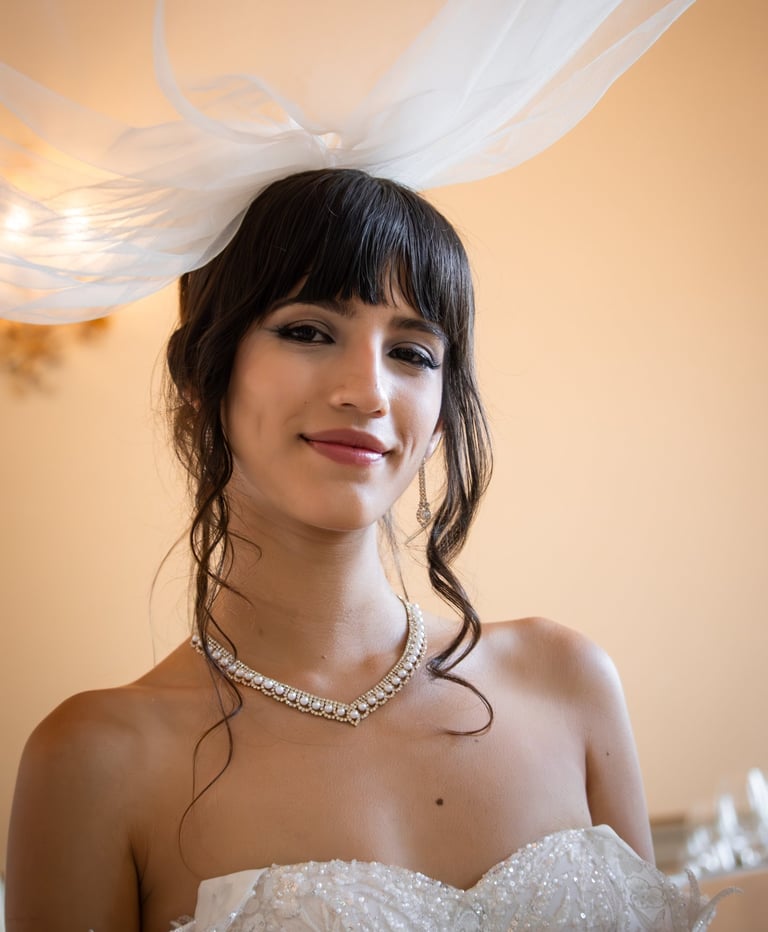 Primo piano elegante di una sposa con cappello di tulle e sorriso leggero, su sfondo caldo.
