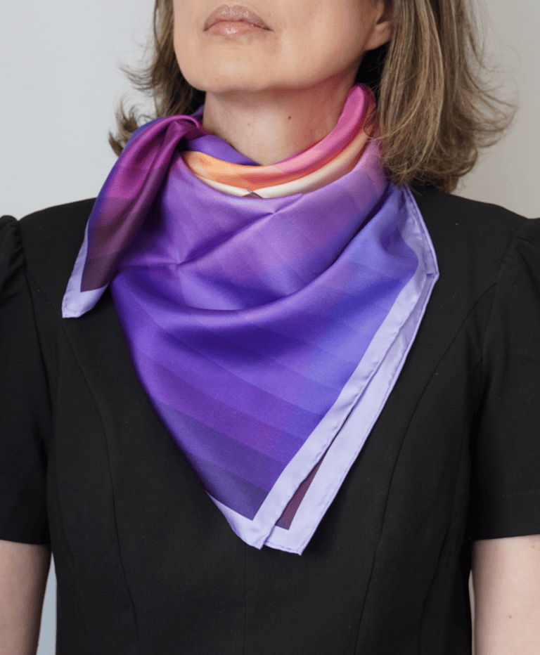 Lenço de seda colorido em tons de lilás e laranja no pescoço e mulher com roupa preta.