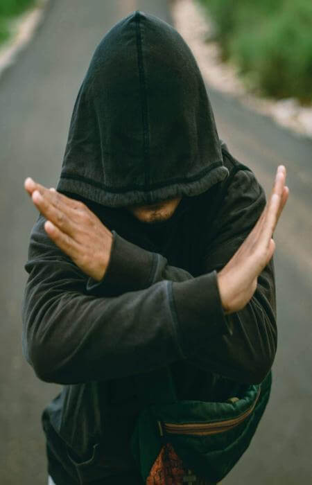 Person in hooded sweatshirt standing on path with arms crossed in an “X” gesture.