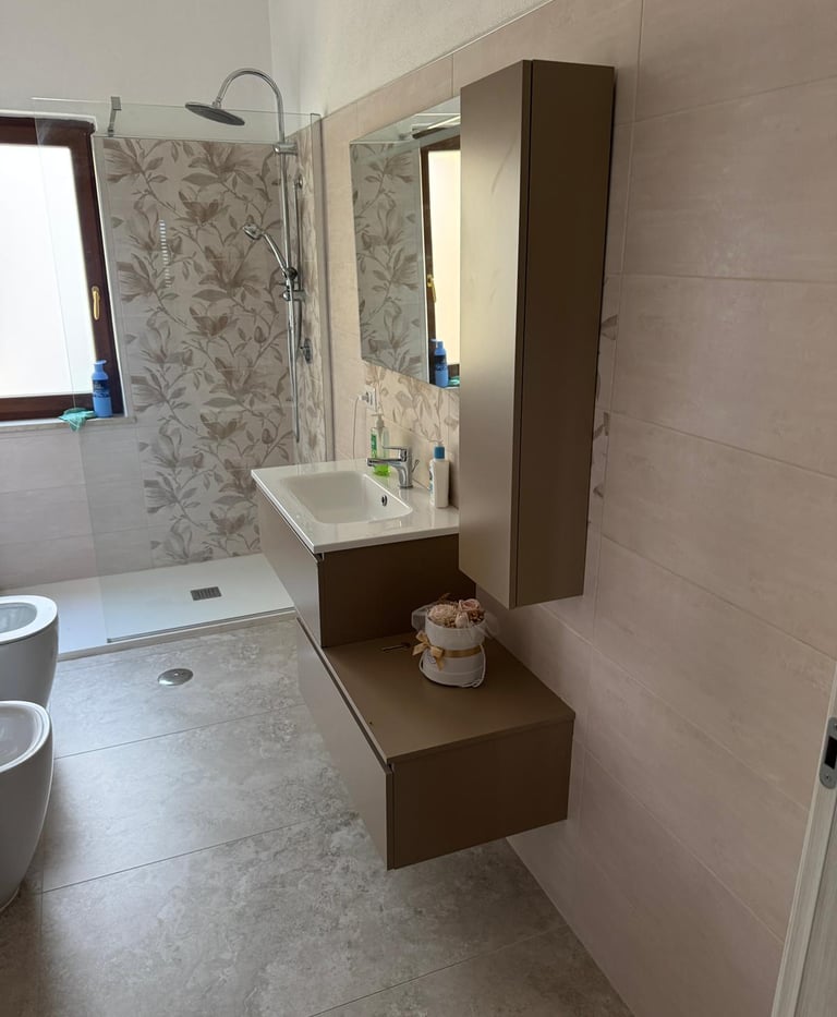 Modern bathroom featuring a floating vanity, walk-in shower with floral tile, and stone flooring.