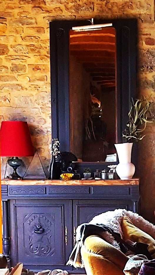 Rustic stone wall featuring a black vintage sideboard and matching framed mirror with elegant home decor.