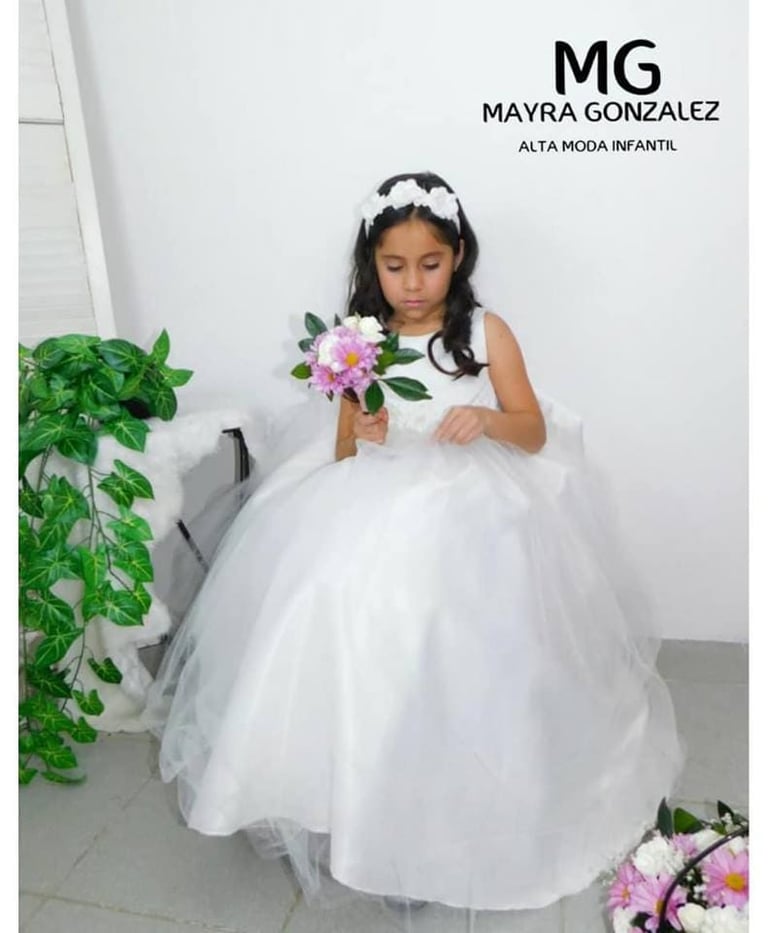 Niña pequeña con un vestido blanco de tul para niña de flores, sosteniendo un ramo.