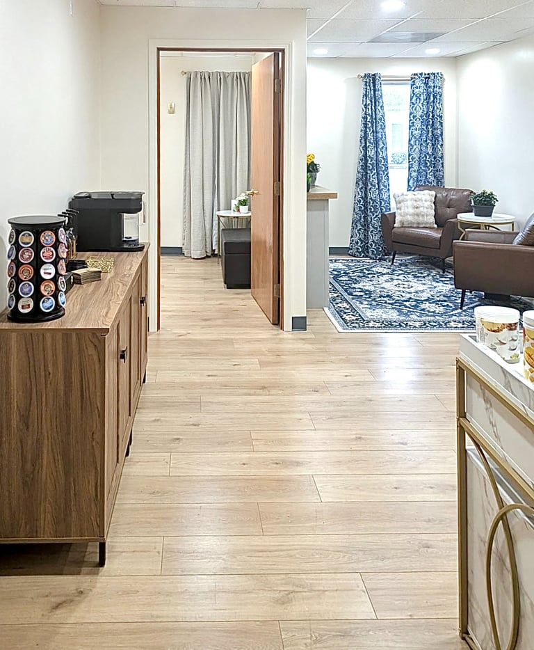 Modern office waiting room with wood floors, blue patterned rug, and brown leather armchairs.