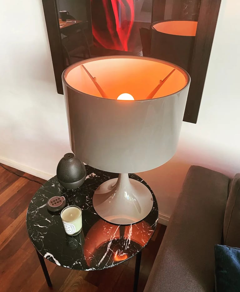 Mesa redonda de soporte para sillón con lámpara de diseño sobre su superficie estilo mármol y cuadro