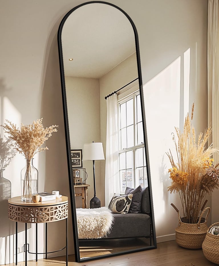 Large arched full-length floor mirror with black metal frame styled in a modern cozy living room.