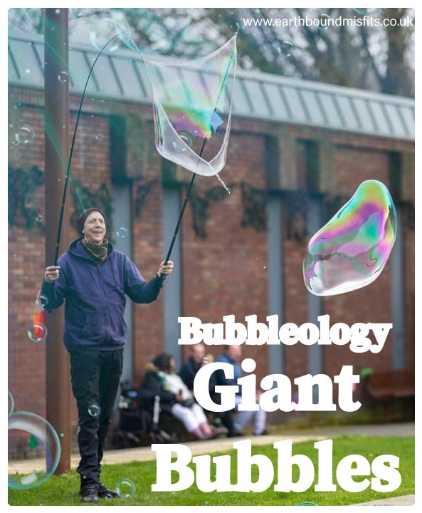 Professional entertainer creating giant iridescent bubbles outdoors with large wands for a bubbleology show.