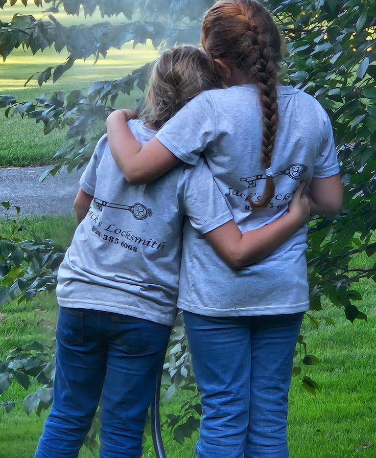 Two daughters hugging outdoors while wearing matching locksmith work shirts