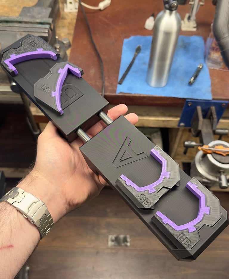 A hand holding a 3D printed mechanical assembly with black and purple plastic components in a workshop.