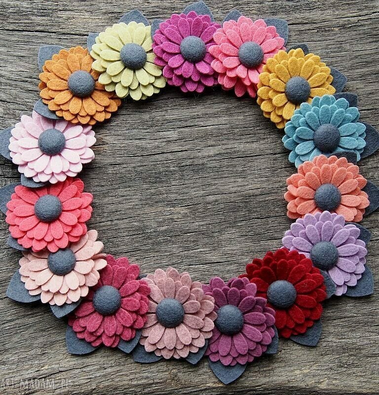 wielokolorowe broszki w kształcie kwiatów ułożone w koło leżą na drewnianej desce