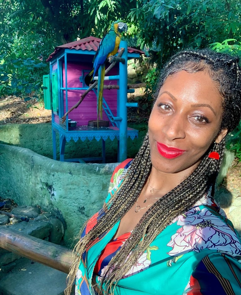A woman with long hair in the Botanic Garden in Deshaies Guadeloupe and a parrot behind her