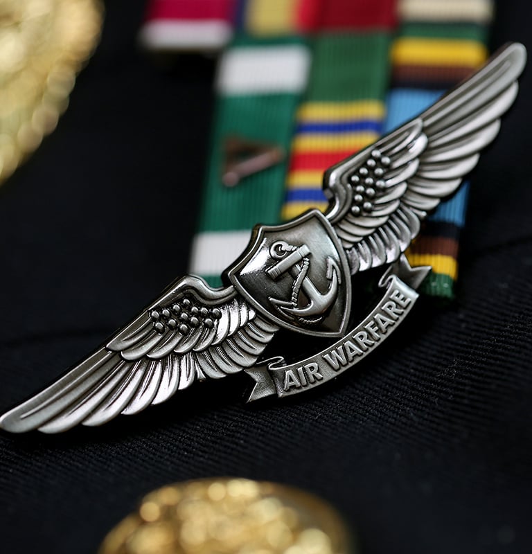 Silver Enlisted Aviation Warfare Specialist insignia pin on a US Navy uniform with ribbons.
