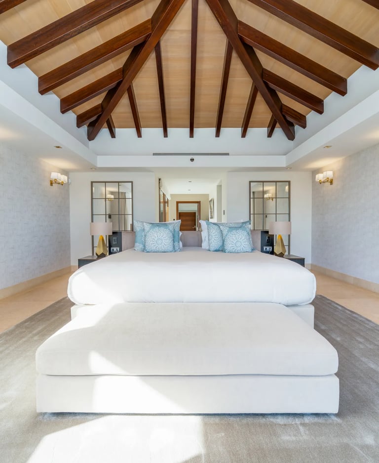 Luxury bedroom suite with a king-size bed, vaulted wood ceiling, and modern tropical decor.