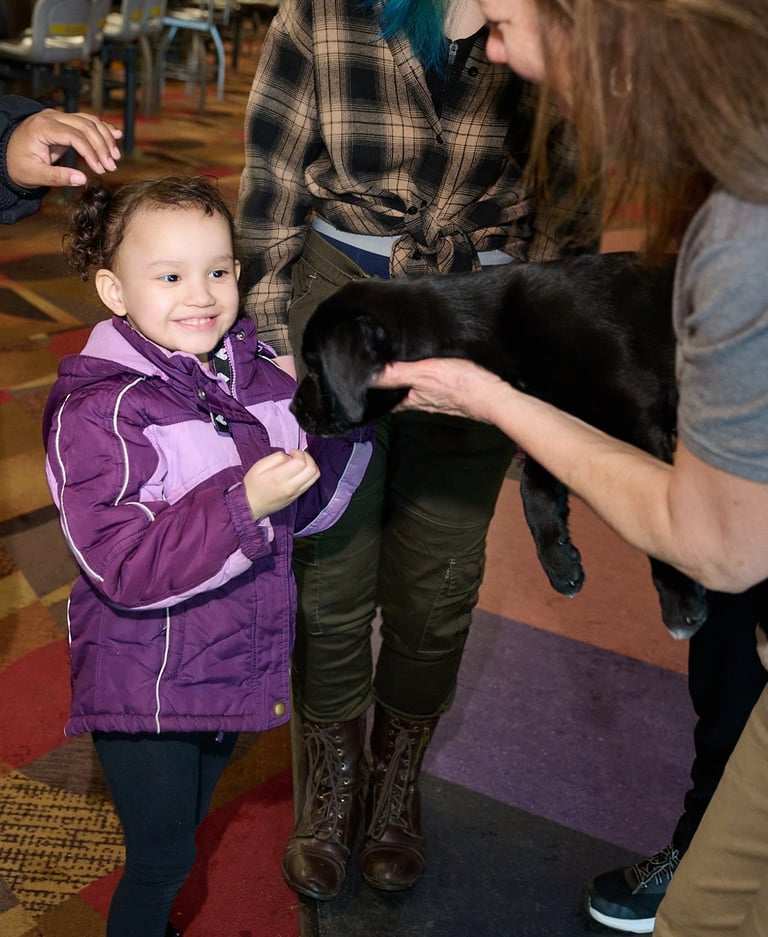 a woman holding a black puppy to a girl in a purple jacket 