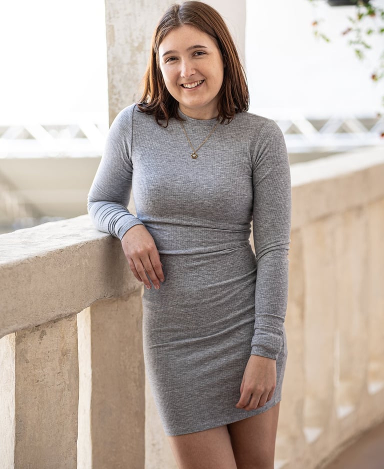 eine Frau in einem grauen Kleid, dass sich locker anlehnt und in die Kamera schaut