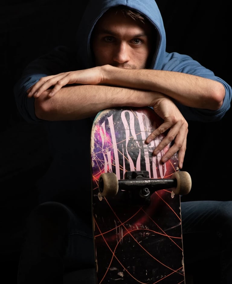 Un jeune homme vêtu d'un sweat à capuche bleu, assis avec un skateboard entre les bras