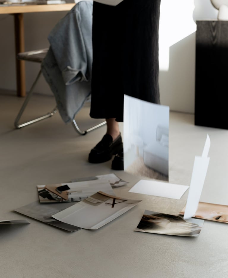A woman in a minimalist studio dropping photography prints onto the floor for a mood board design.
