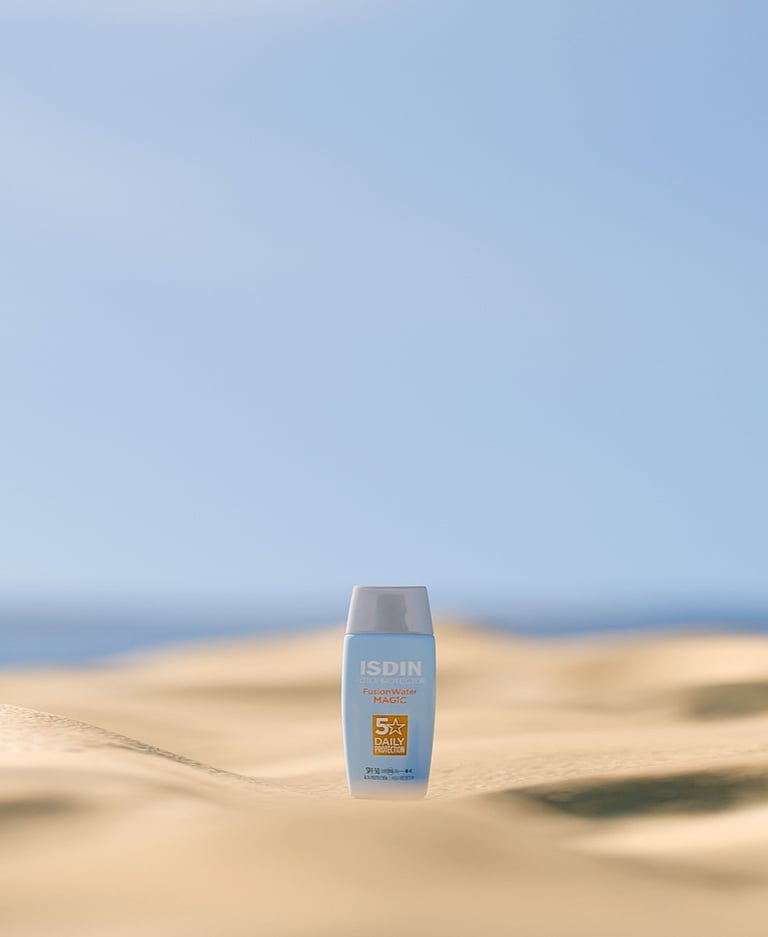 Bote de crema solar de la marca ISDIN en la playa.
