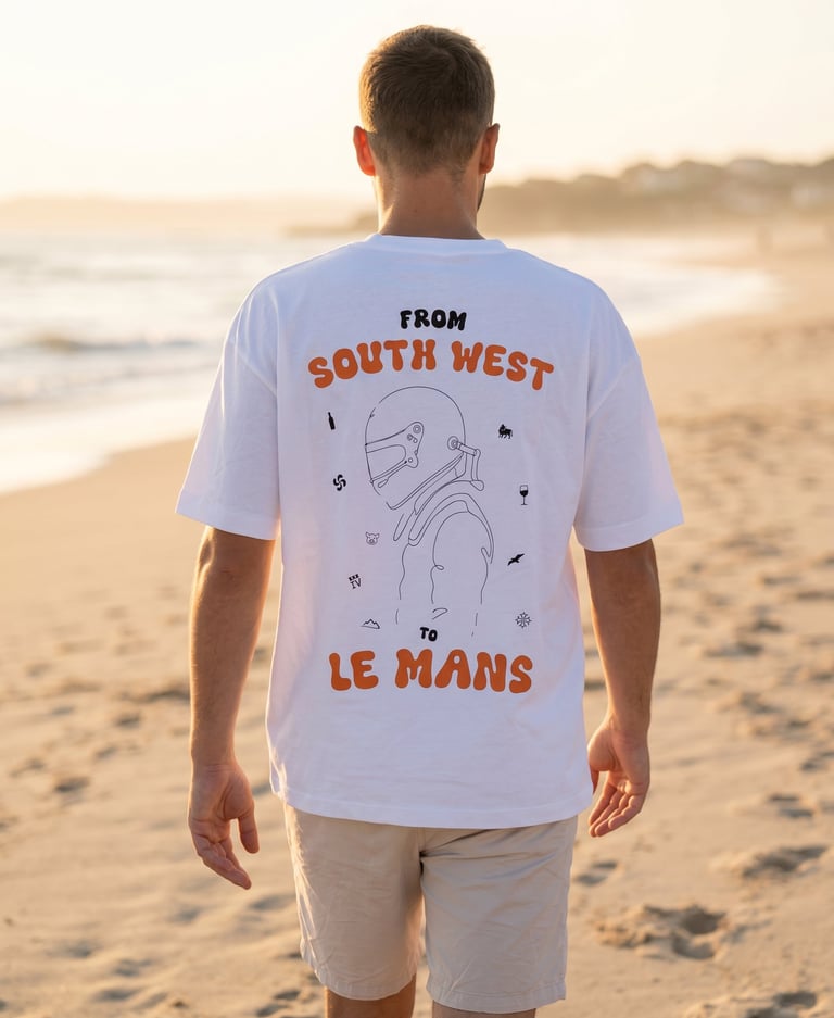 A man wearing a white graphic t-shirt with orange text and a racing driver illustration on a beach.