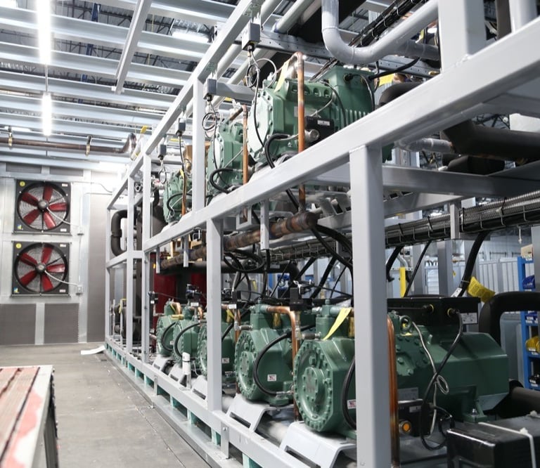 Industrial refrigeration rack system with green semi-hermetic compressors and cooling fans.