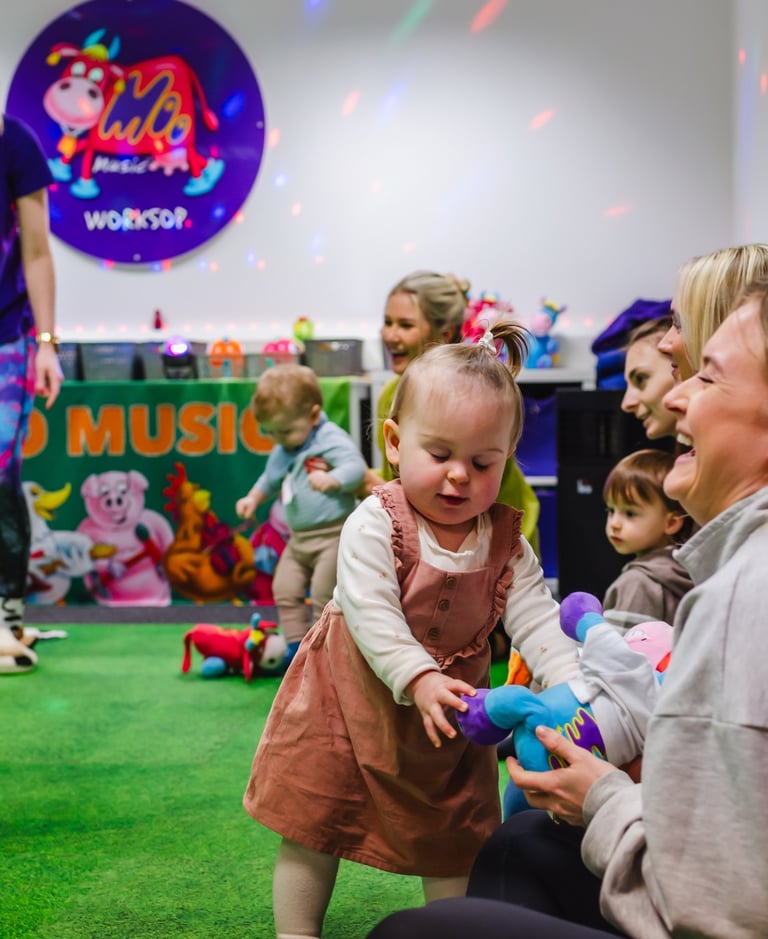 A young Mini Moo attendee and her Mum smiling and laughing, playing with a soft toy.