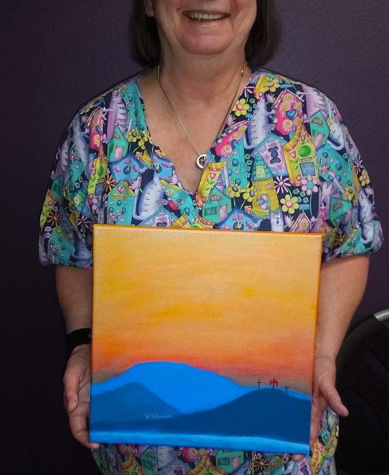 a woman holding a painting of a mountain scene with three crosses