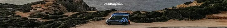 A Roadsurfer camper van parked on a rugged cliff overlooking the ocean at sunset.
