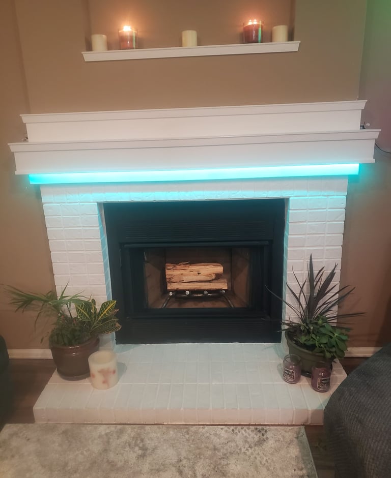 Modern white painted brick fireplace featuring teal LED mantel lighting, decorative candles, and indoor plants.