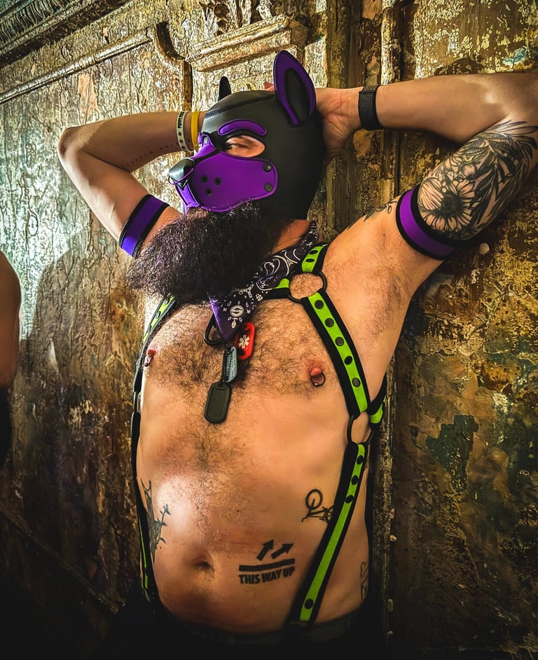 Shirtless man in pup mask, leaning against a bar wall