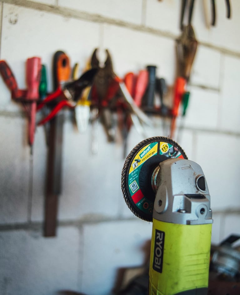 A close-up of a Ryobi power tool, specifically a grinding machine, with various tools hanging on the wall in the background.