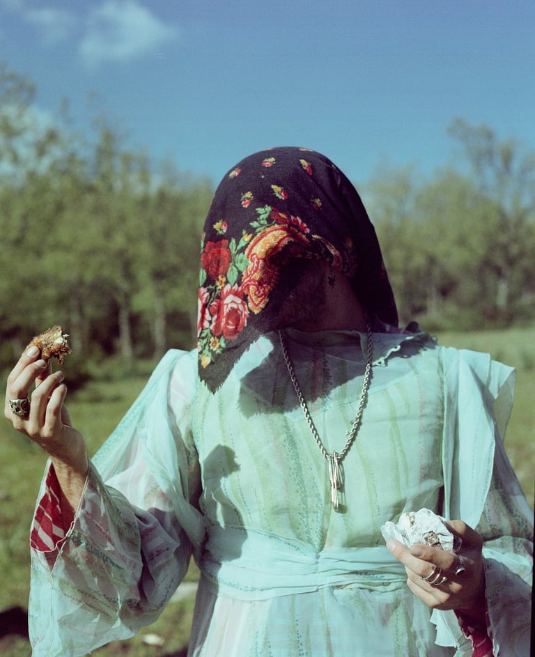 Person in vintage floral headscarf and light blue gown holding food in an outdoor setting.