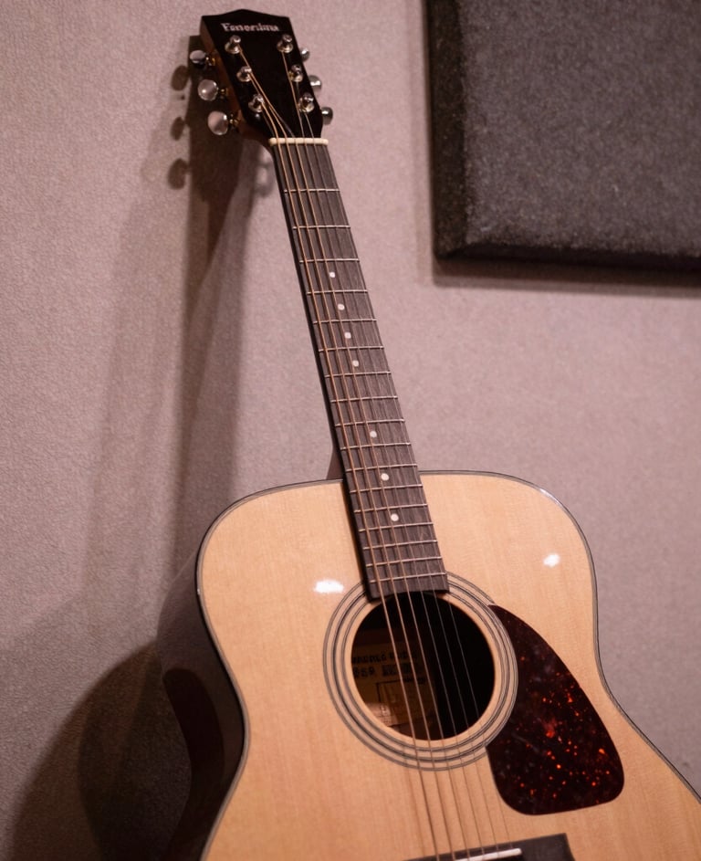 A moody close-up of an acoustic guitar leaning against a textured wall in a Venezuelan recording studio, warm antique white and dusty rose lighting, authentic musical atmosphere.