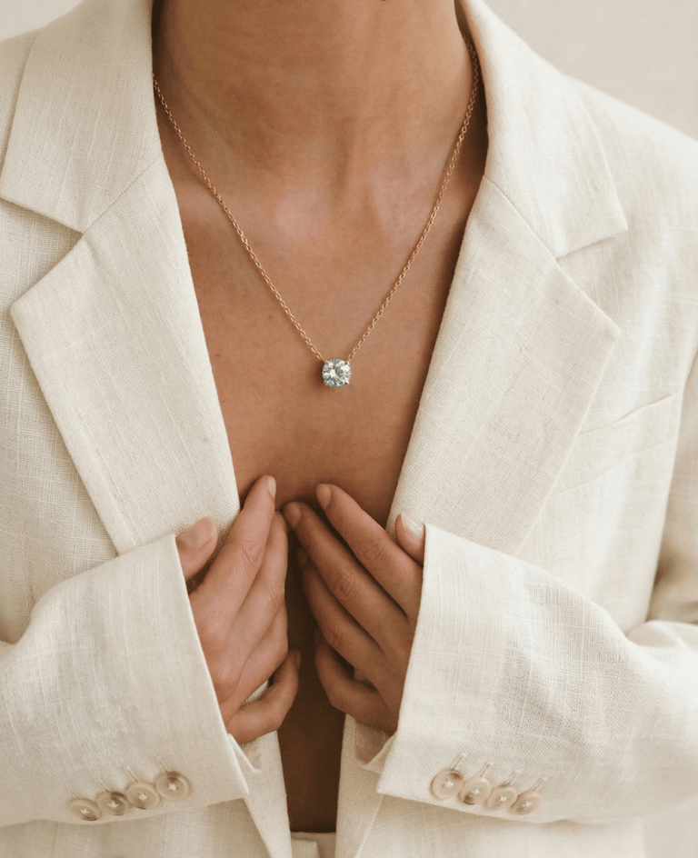 Elegant woman wearing a solitaire diamond pendant on a gold chain with a white linen blazer.