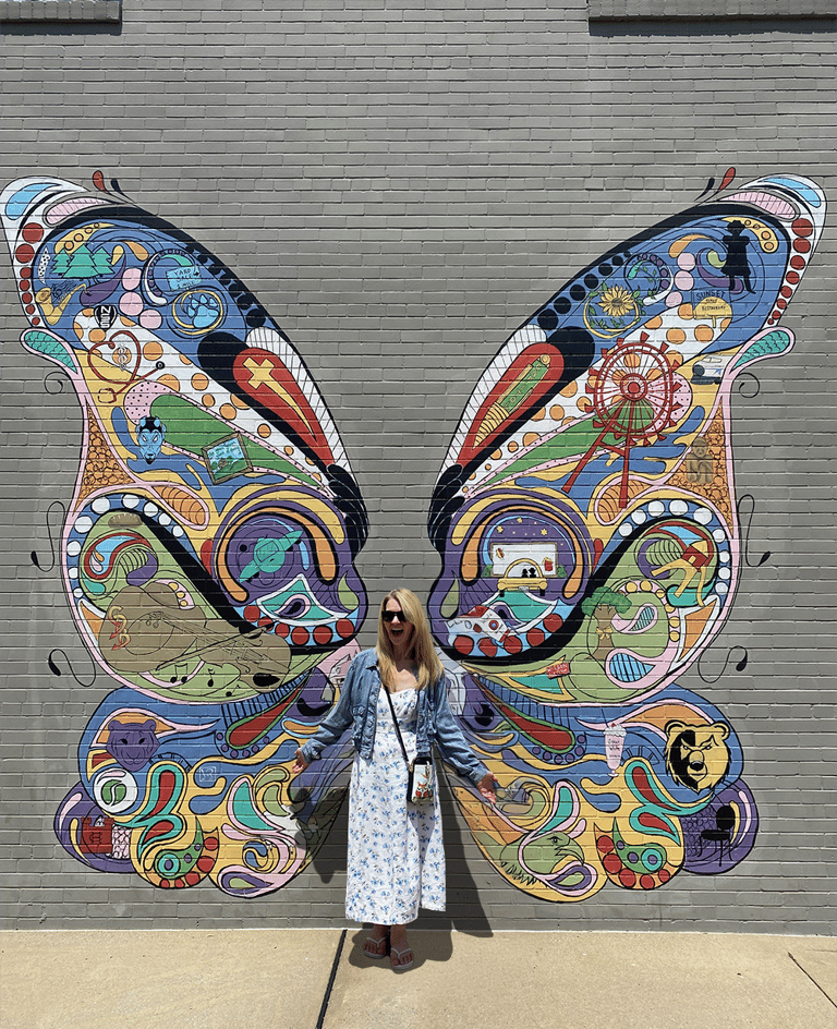 Nini standing against a wall with a mural of butterfly wings