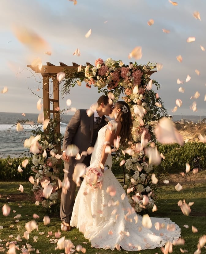 bride and groom kissing in front of a wedding arbor at Cuvier Park pink and white flowers