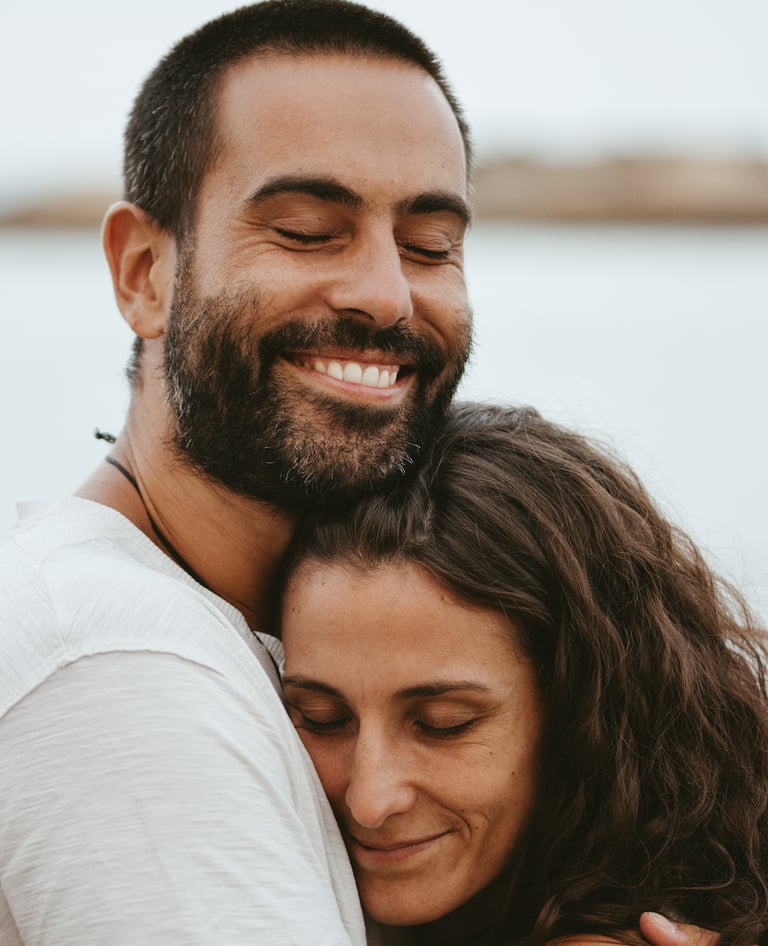 Smiling happy couple embracing outdoors with eyes closed in a romantic hug at the beach.