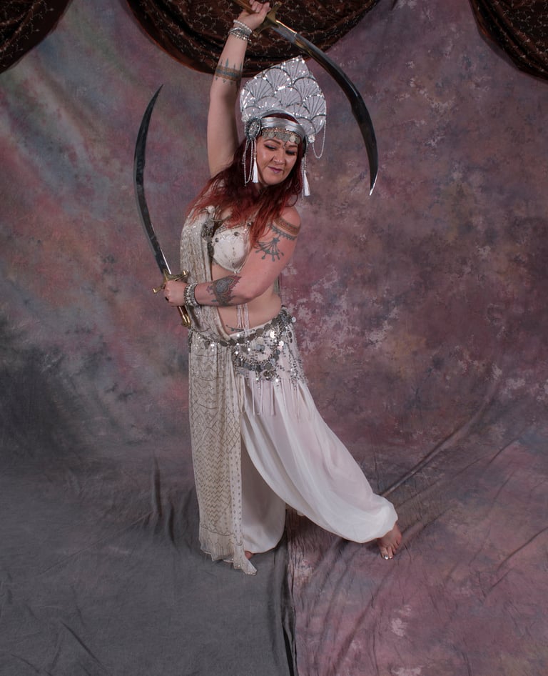 Bellydancer Shahravar with double swords wearing white assuit costume with coin bedlah