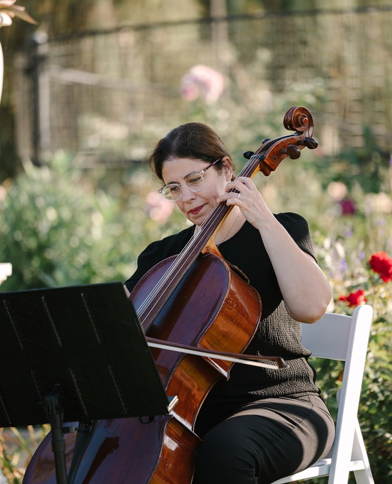 Professional cellist playing cello during an outdoor garden wedding ceremony.