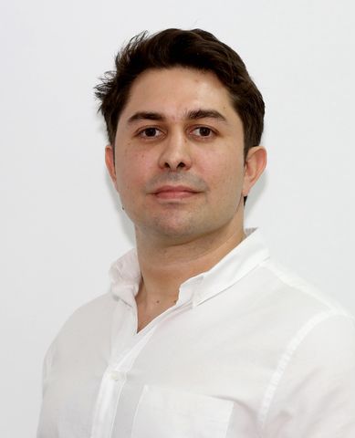 Professional headshot of a man with brown hair wearing a white button-down shirt against a plain background.