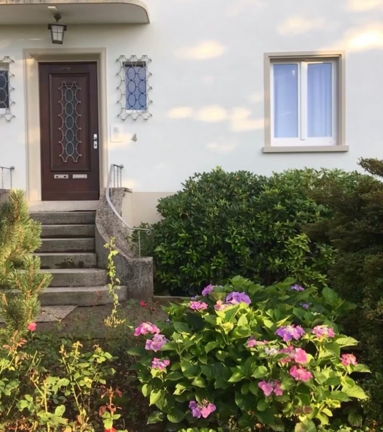 ein Hauseingang mit Treppe und einer Holztür von Büschen und Blumen umgeben