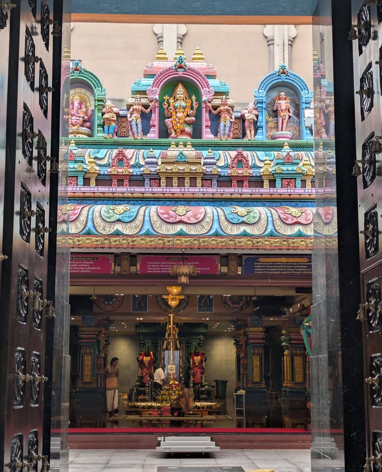 View through open temple doors of colorful Hindu deities and the interior of Sri Mariamman Temple.